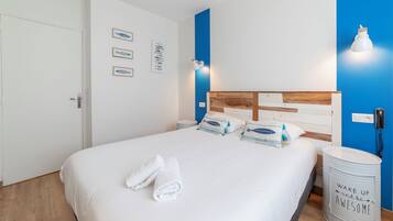 A neatly made bed with white linens and two rolled towels, a wooden headboard, and a wall with framed fish illustrations.