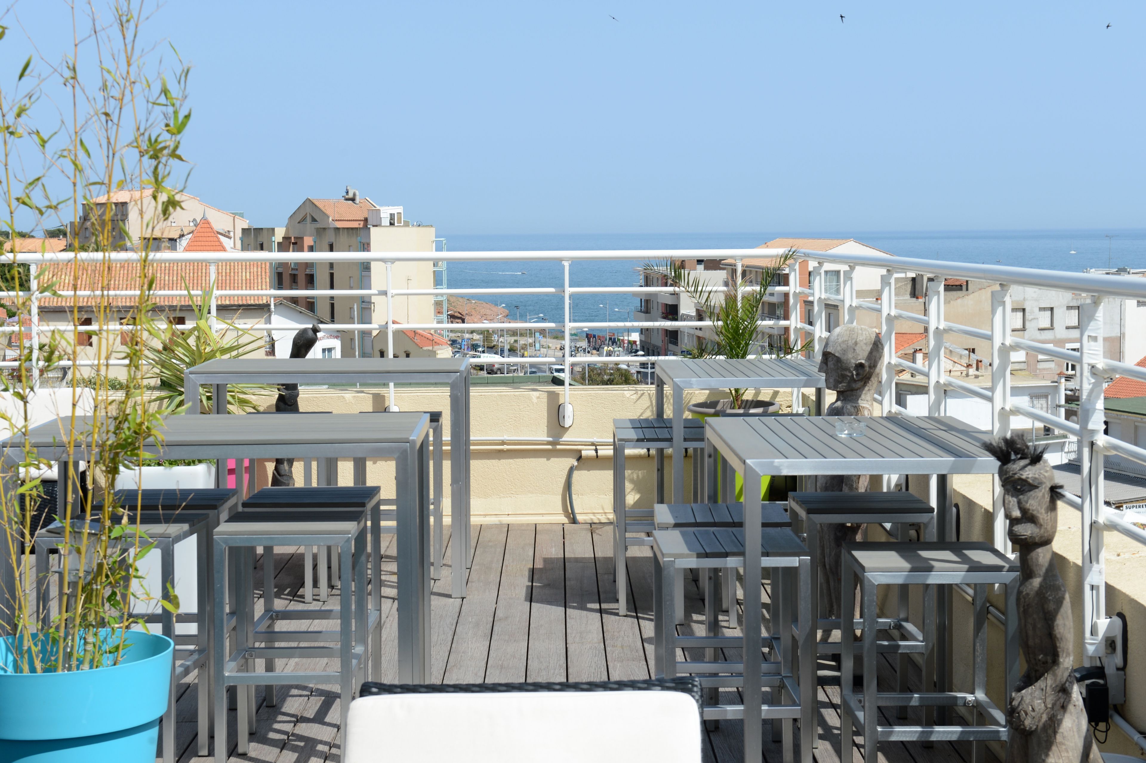 Eine Dachterrasse mit Sitzgelegenheiten im Freien, Blick auf das Meer und Gebäude im Hintergrund.