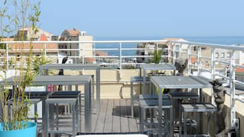 Eine Dachterrasse mit Sitzgelegenheiten im Freien, Blick auf das Meer und Gebäude im Hintergrund.