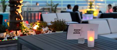 A table with a menu card and a candle, surrounded by decorative plants and a stone sculpture.