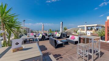 Un salon sur le toit avec des espaces de détente en plein air, un bar et une vue sur la mer.