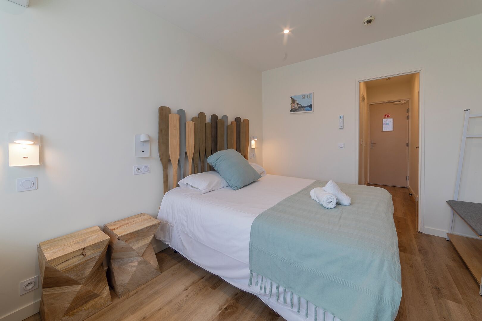 A bedroom with a wooden headboard, a bed with white bedding, a teal throw blanket, and two bedside tables.