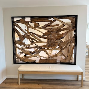A room with a wooden art installation, a white bench, and a view of a bed with a white headboard. - Hôtel Impérial (Sète)