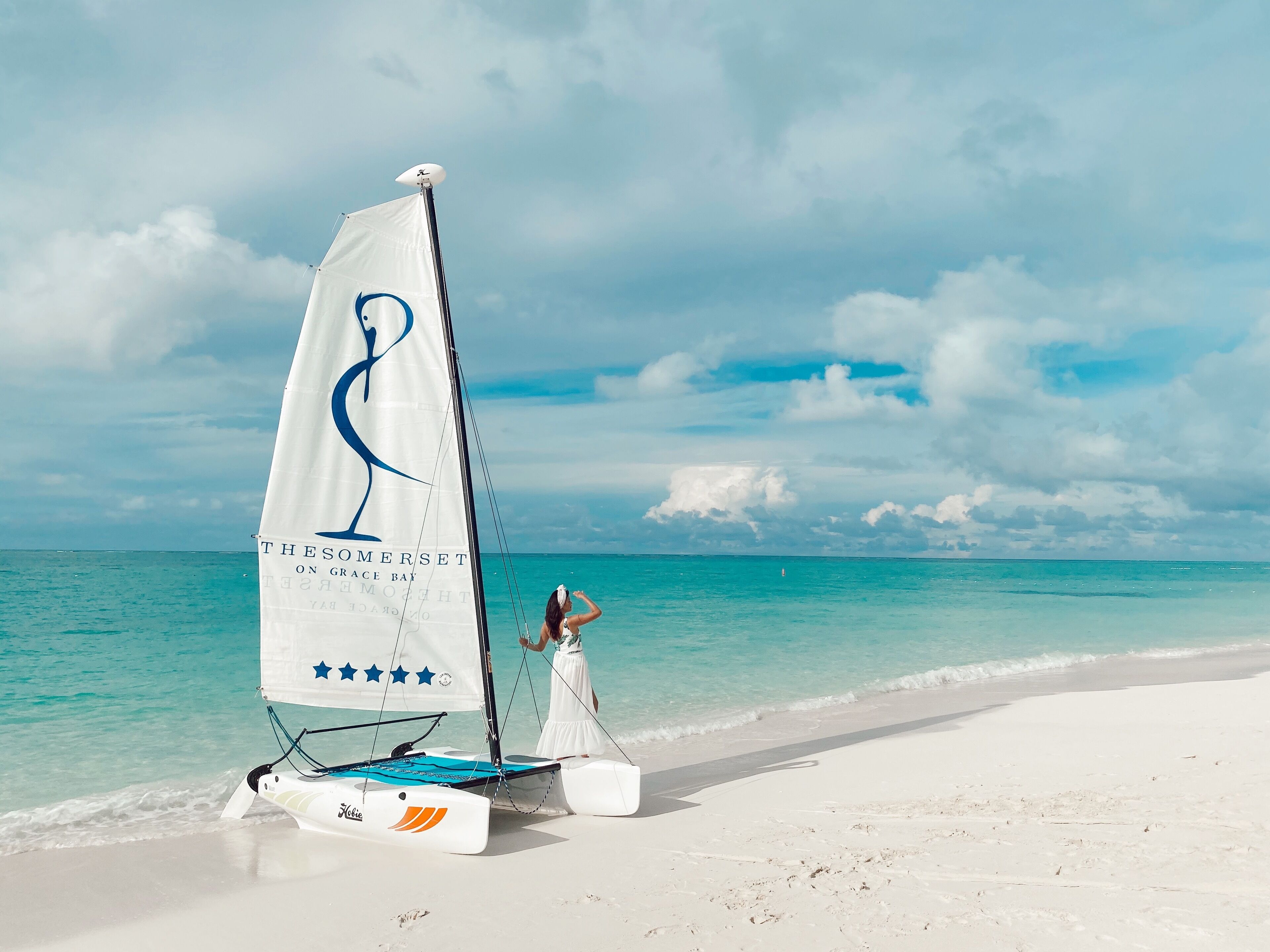 Een zeilboot met een witte zeil en blauwe letters op het strand.