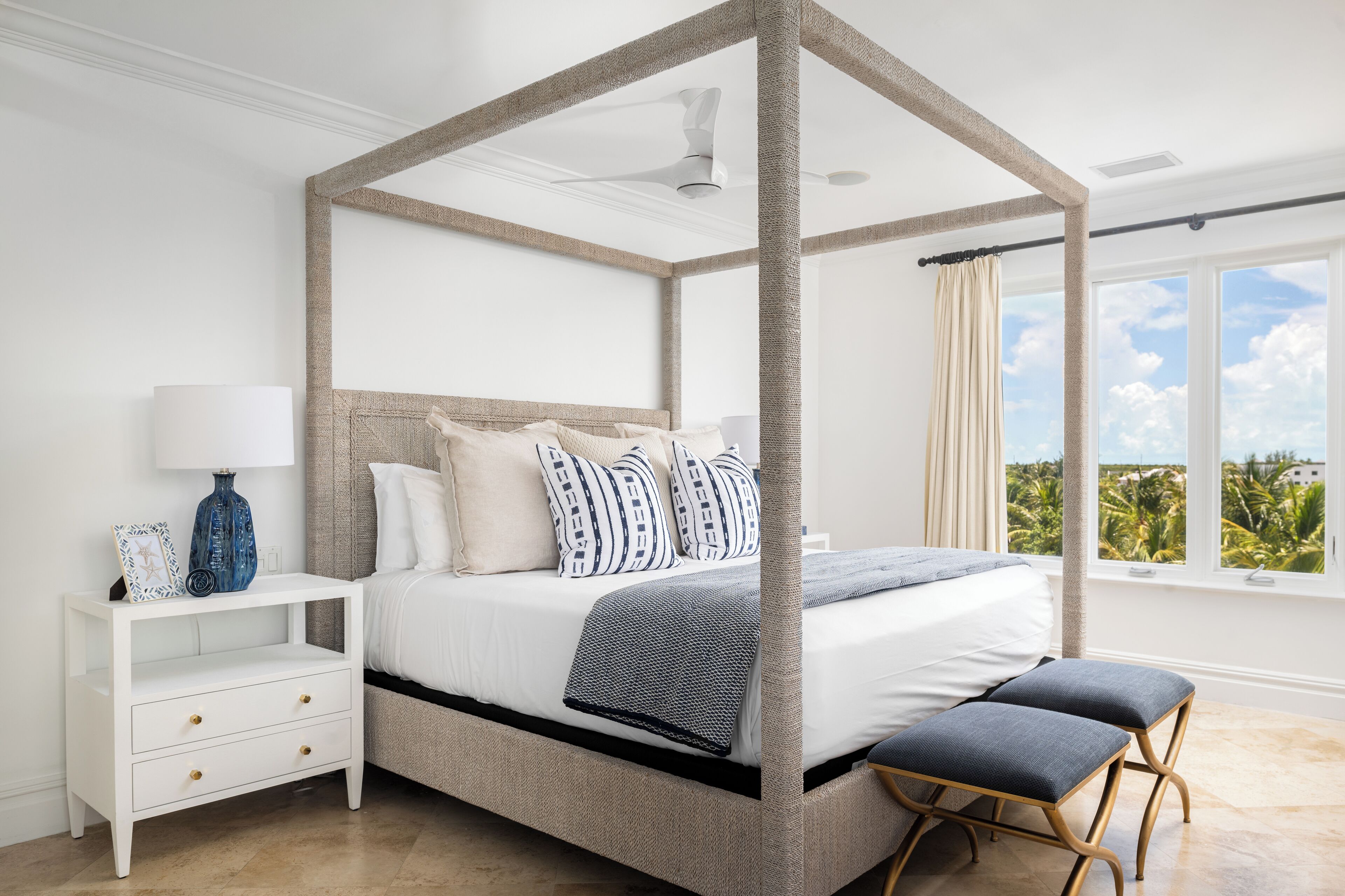 Ein Schlafzimmer mit Himmelbett, Nachttisch mit Schubladen, einer Bank und einem Fenster mit Blick auf Grünflächen.