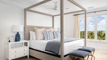 Ein Schlafzimmer mit Himmelbett, Nachttisch mit Schubladen, einer Bank und einem Fenster mit Blick auf Grünflächen.