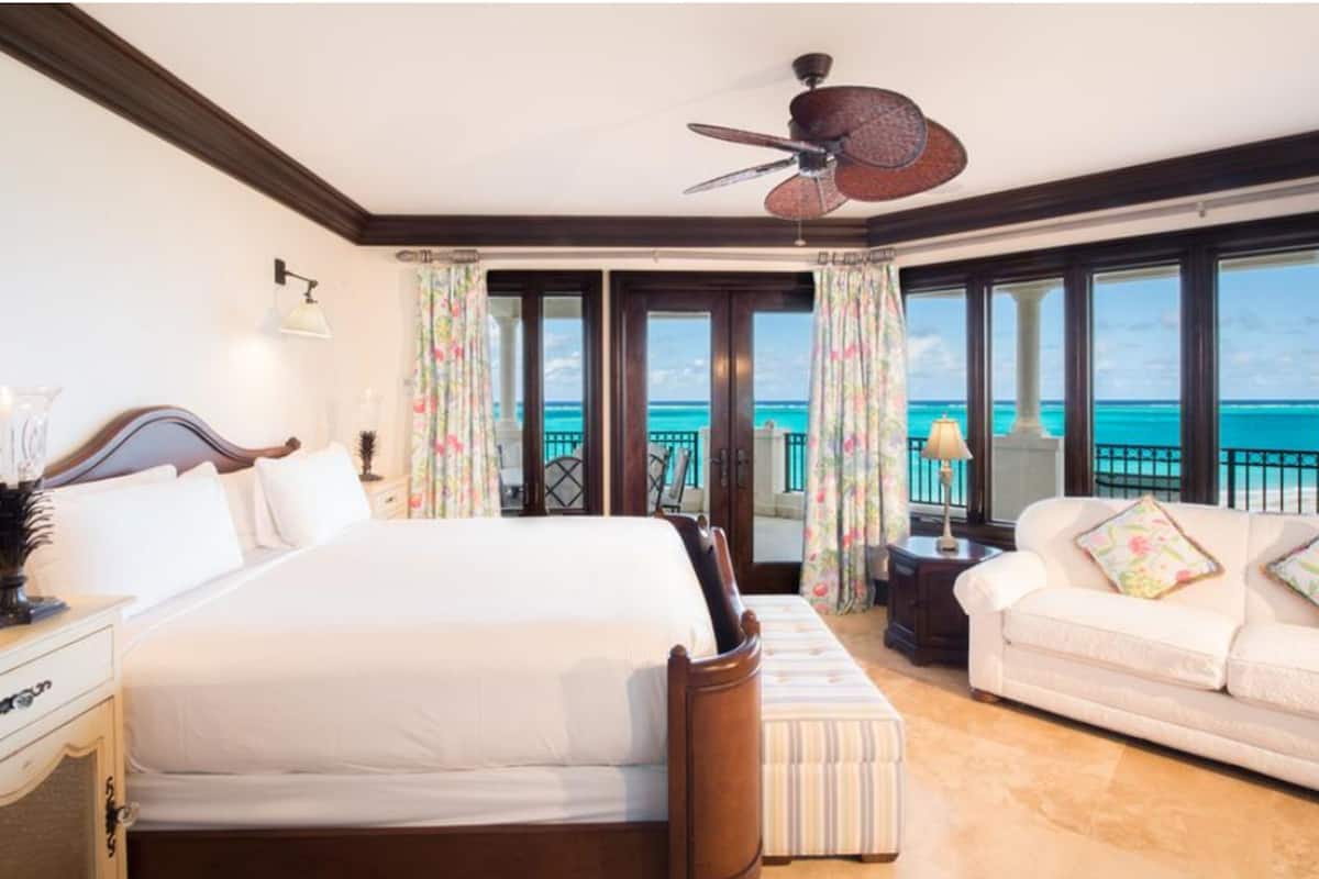Une chambre d’hôtel avec un grand lit, un canapé, un ventilateur de plafond et une vue sur l’océan.