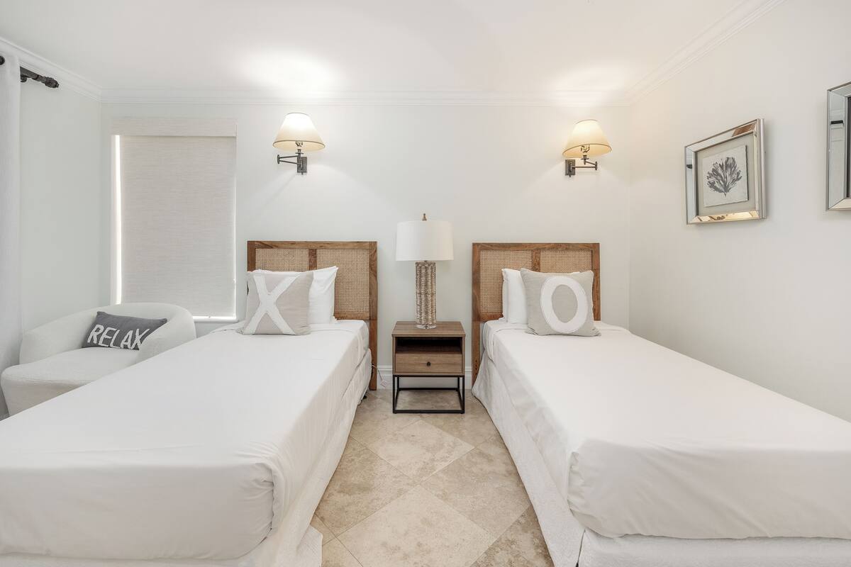 Une chambre d’hôtel avec deux lits simples, une table de chevet avec une lampe et un tableau accroché au mur.