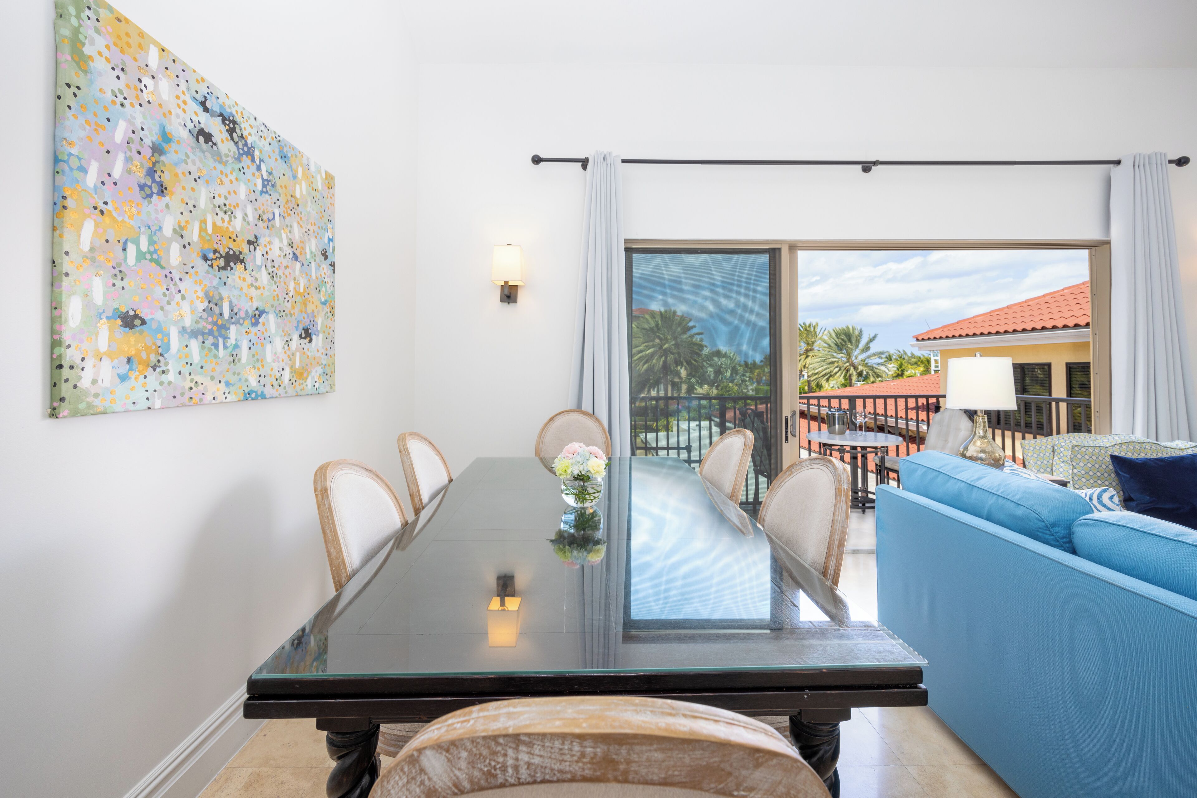 A modern dining area with a glass table, white chairs, and a blue sofa.