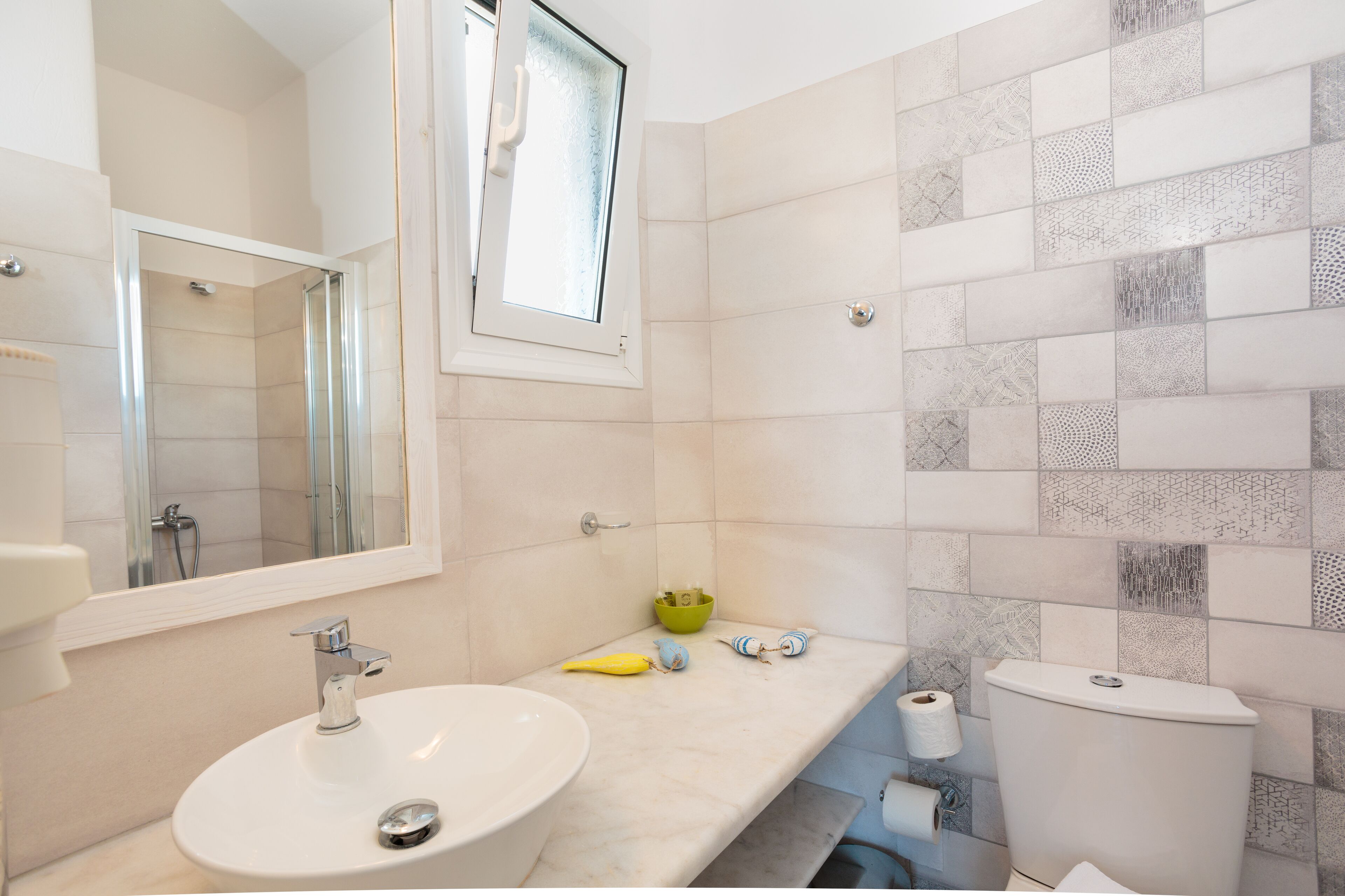 A bathroom with a sink, mirror, toilet, and patterned tiles.