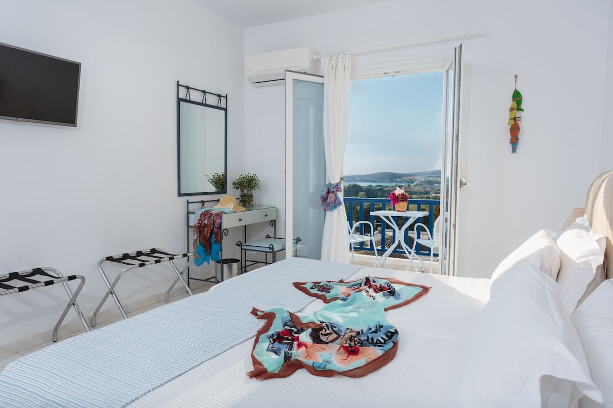 A hotel room with a bed, a desk, a chair, and a balcony with a view.