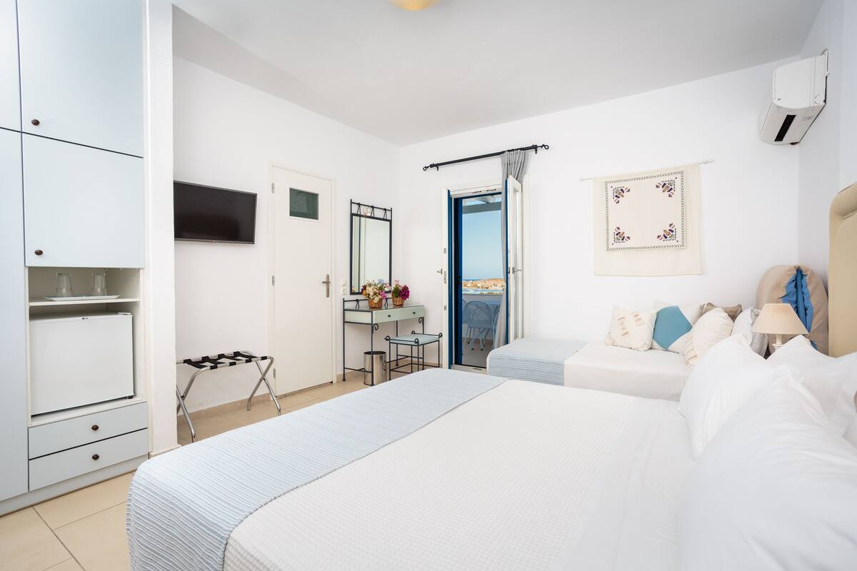 A bedroom with two beds, a desk, a wardrobe, and a TV.