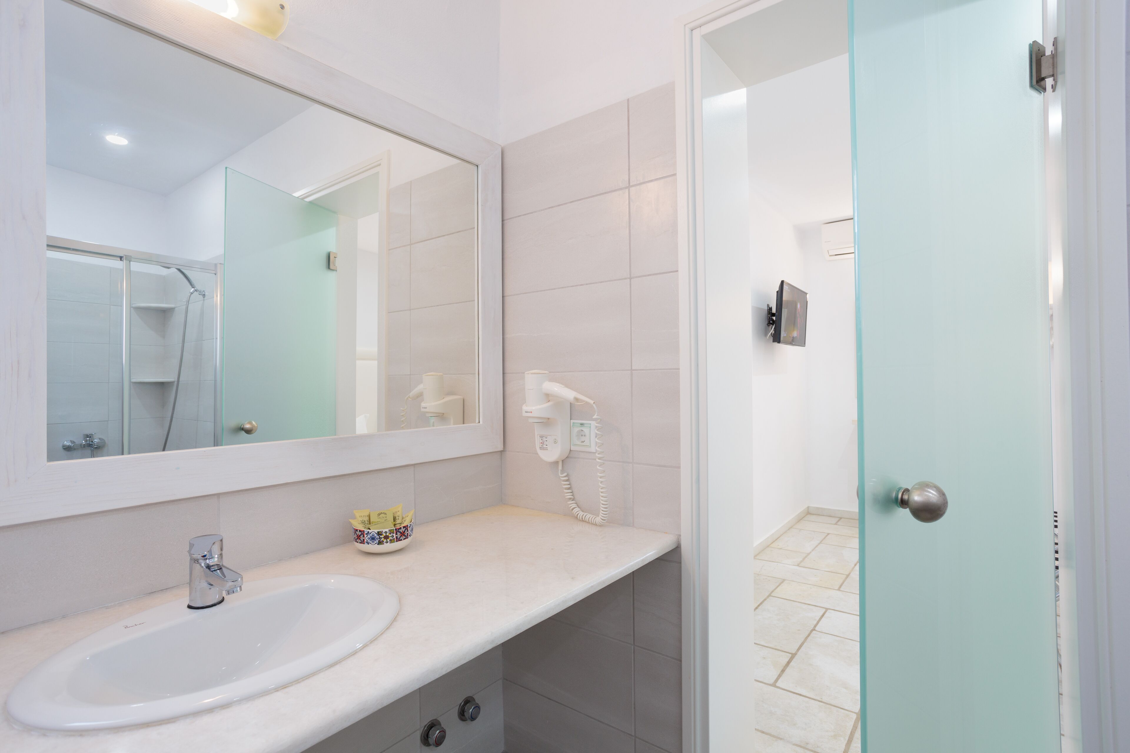 A bathroom with a white sink, a mirror, and a glass shower door.
