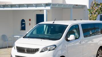 A white van parked in front of a white building with a blue door and a small window with a blue frame.