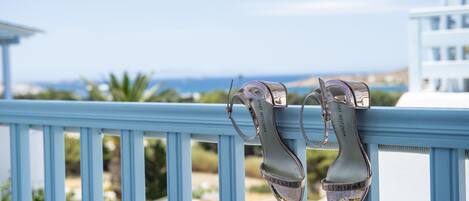 A pair of high-heeled shoes on a balcony railing with a view of the ocean and buildings in the background.