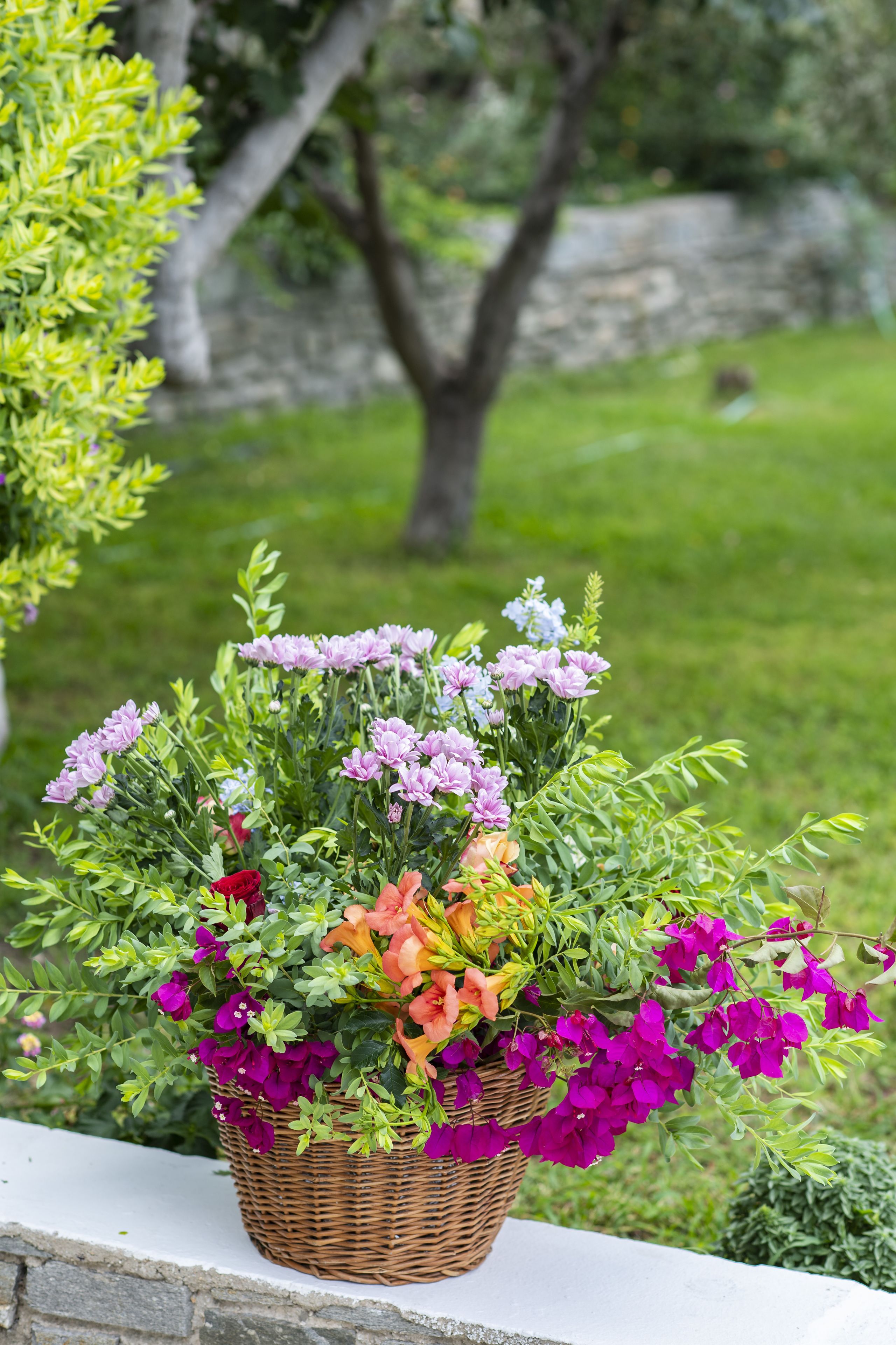 A wicker basket filled with colorful flowers on a stone ledge.