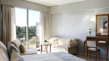 Habitació d'hotel amb llit, escriptori, cadira i una finestra gran que ofereix vistes a la vegetació.