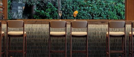 Un área de bar con cuatro taburetes de madera, una copa de cóctel y vistas a la vegetación a través de una ventana.