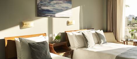 A hotel room with two beds, a painting on the wall, a window with curtains, and a small table with a vase.
