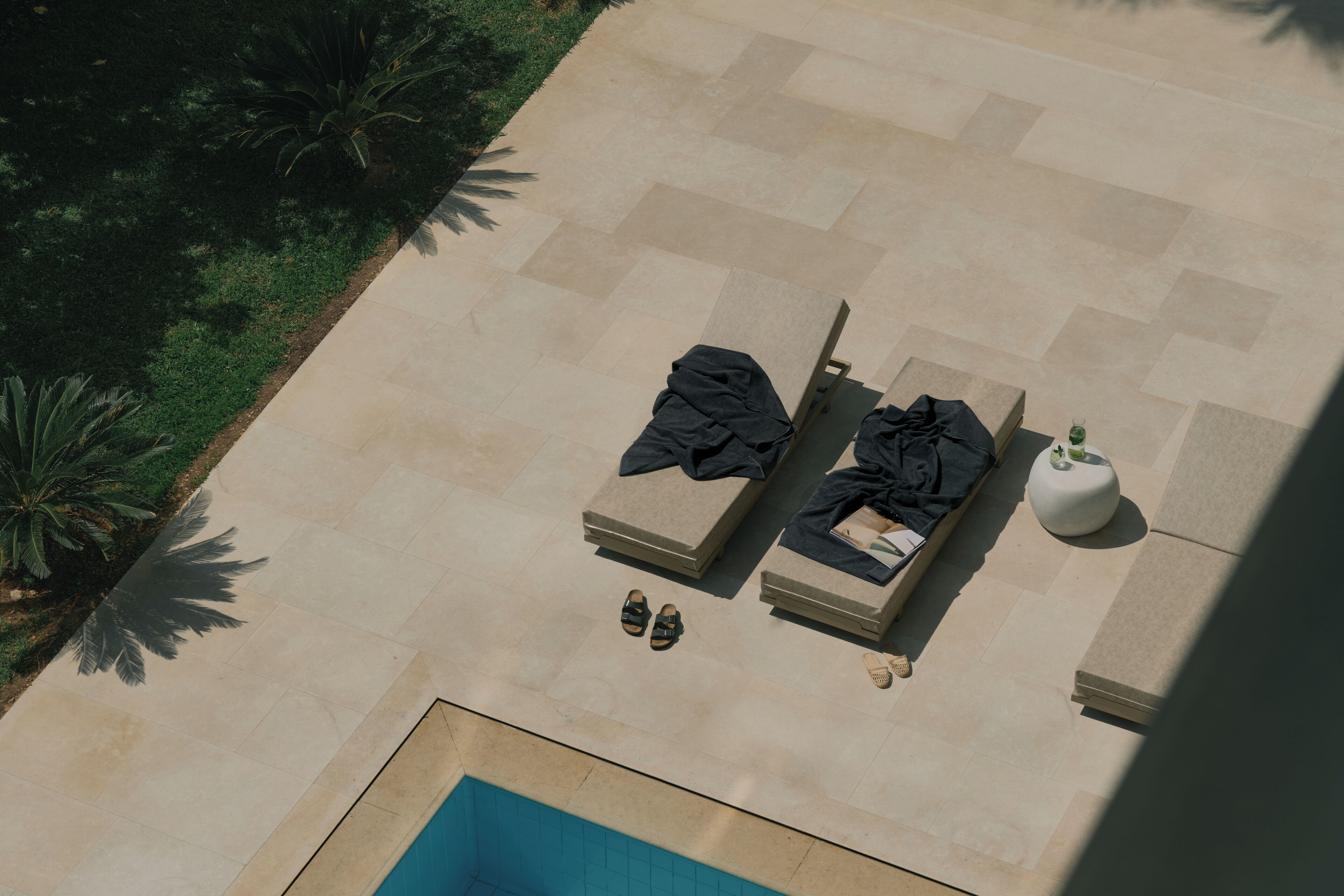 An aerial view of a poolside area with two sun loungers, a small table, and a potted plant.