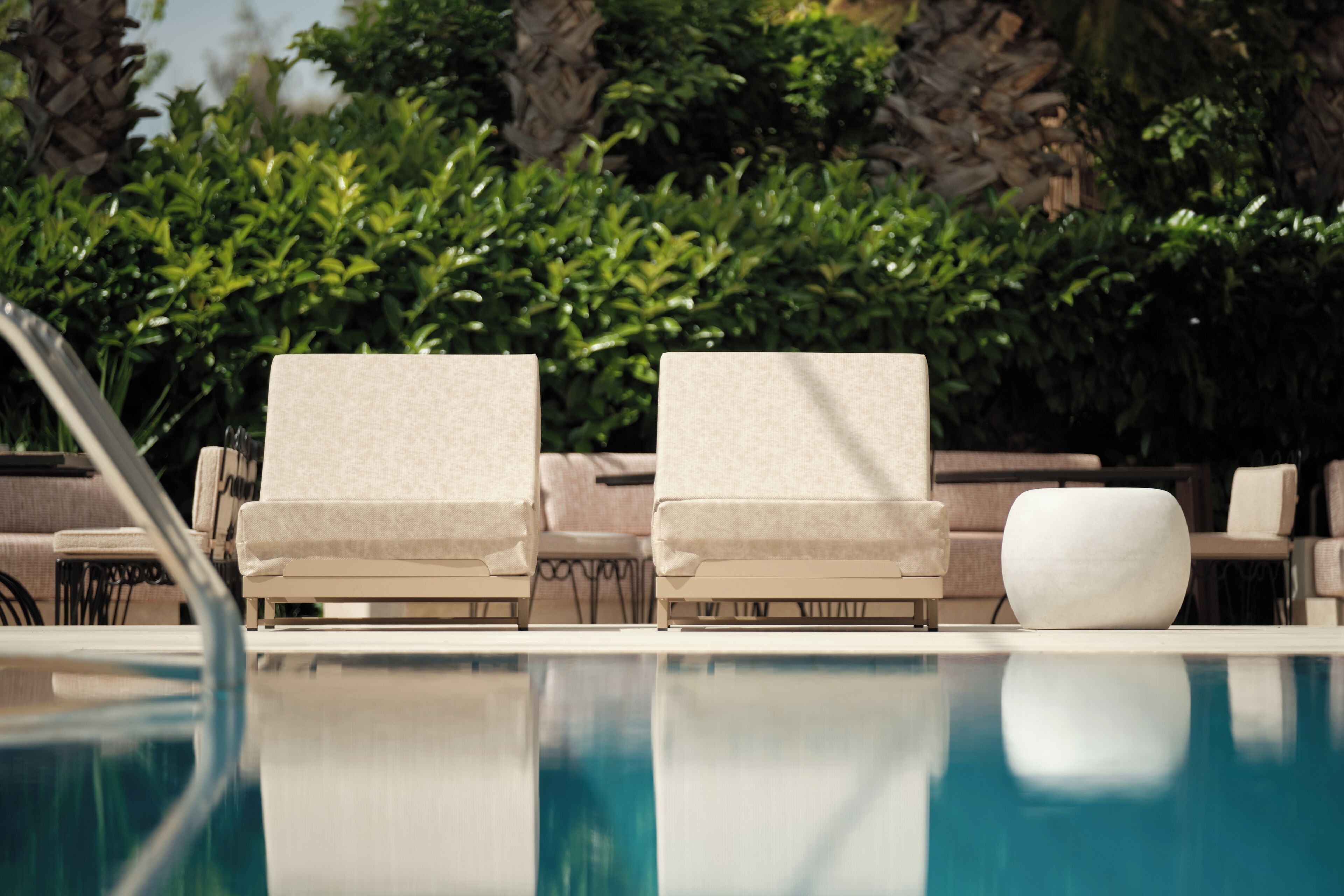 A poolside area with two beige lounge chairs and a white ottoman.