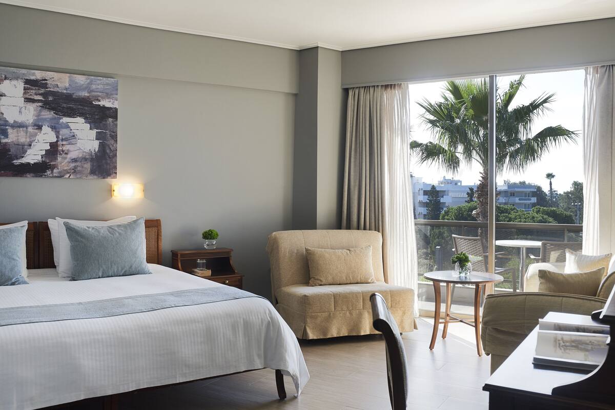 A hotel room with a bed, a sofa, a chair, a small table, and a piano.