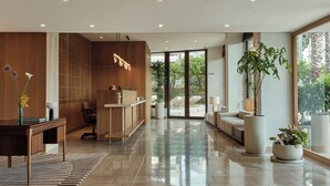 A modern reception area with a wooden reception desk, a seating area with a sofa, and large potted plants. - Golden Sun (Glyfada)