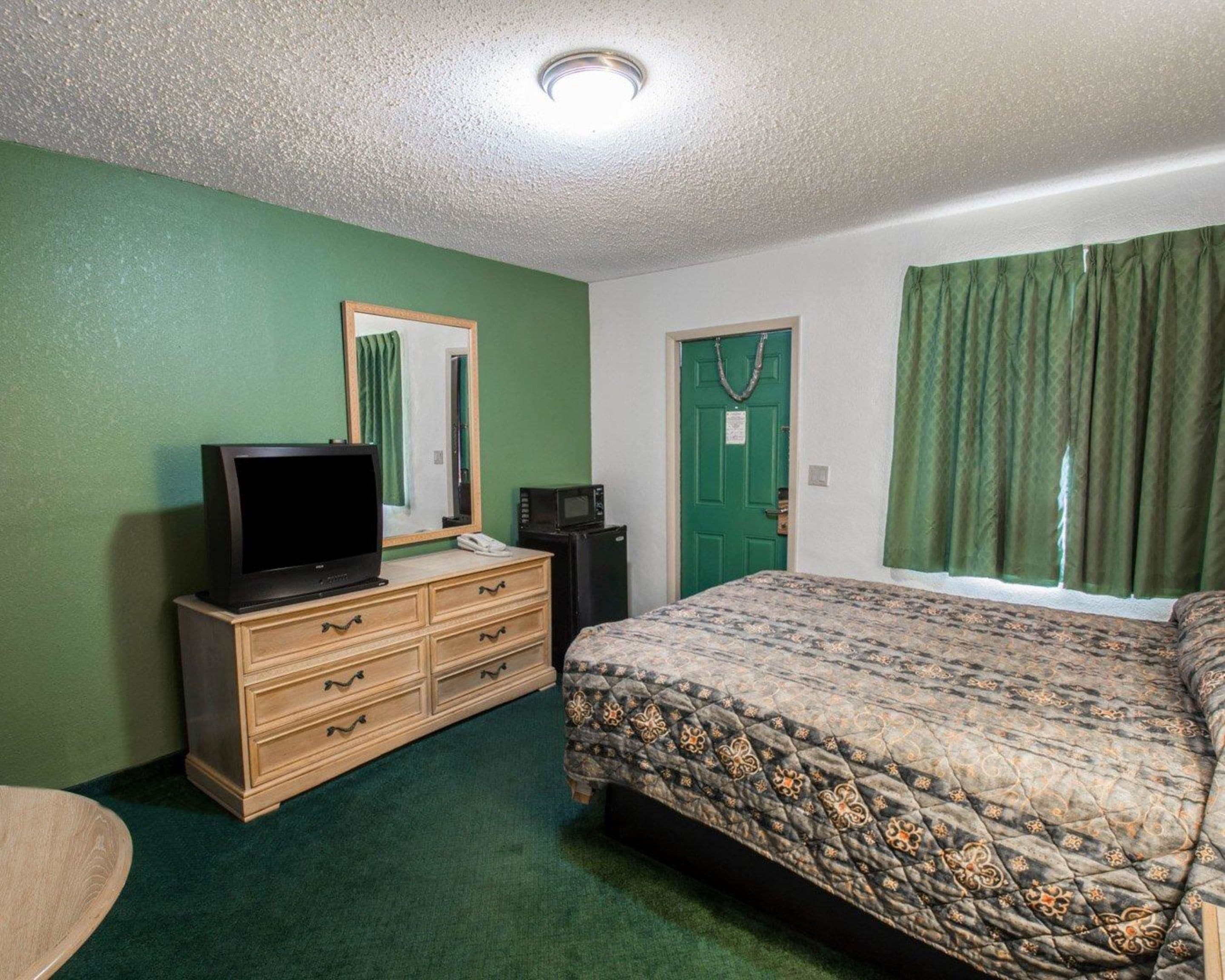 A room with a bed, a dresser, a television, a microwave, and a green door.
