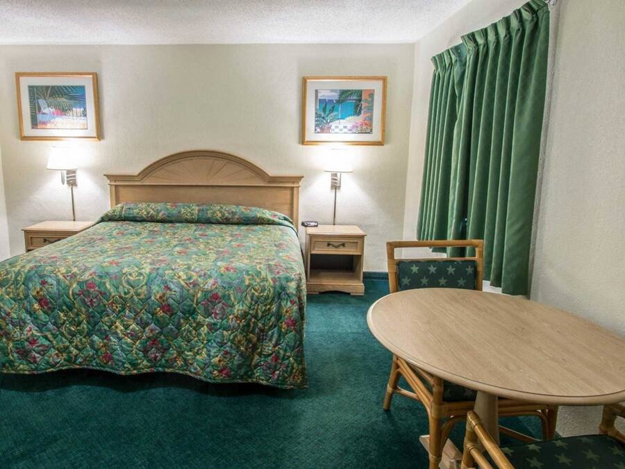 Ein Hotelzimmer mit einem Bett, Nachttischen, einem Sessel, einem Tisch und zwei gerahmten Bildern an der Wand.
