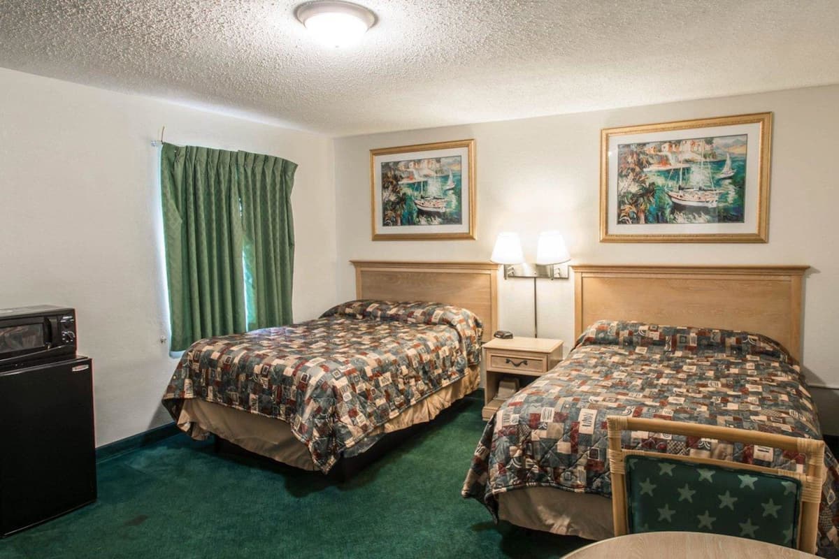 A hotel room with two beds, a desk, a chair, a lamp, and a refrigerator.
