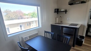 A compact kitchen with a window, a sink, a stove, and a small dining area with chairs. - Richland Inn and Suites (Richland)