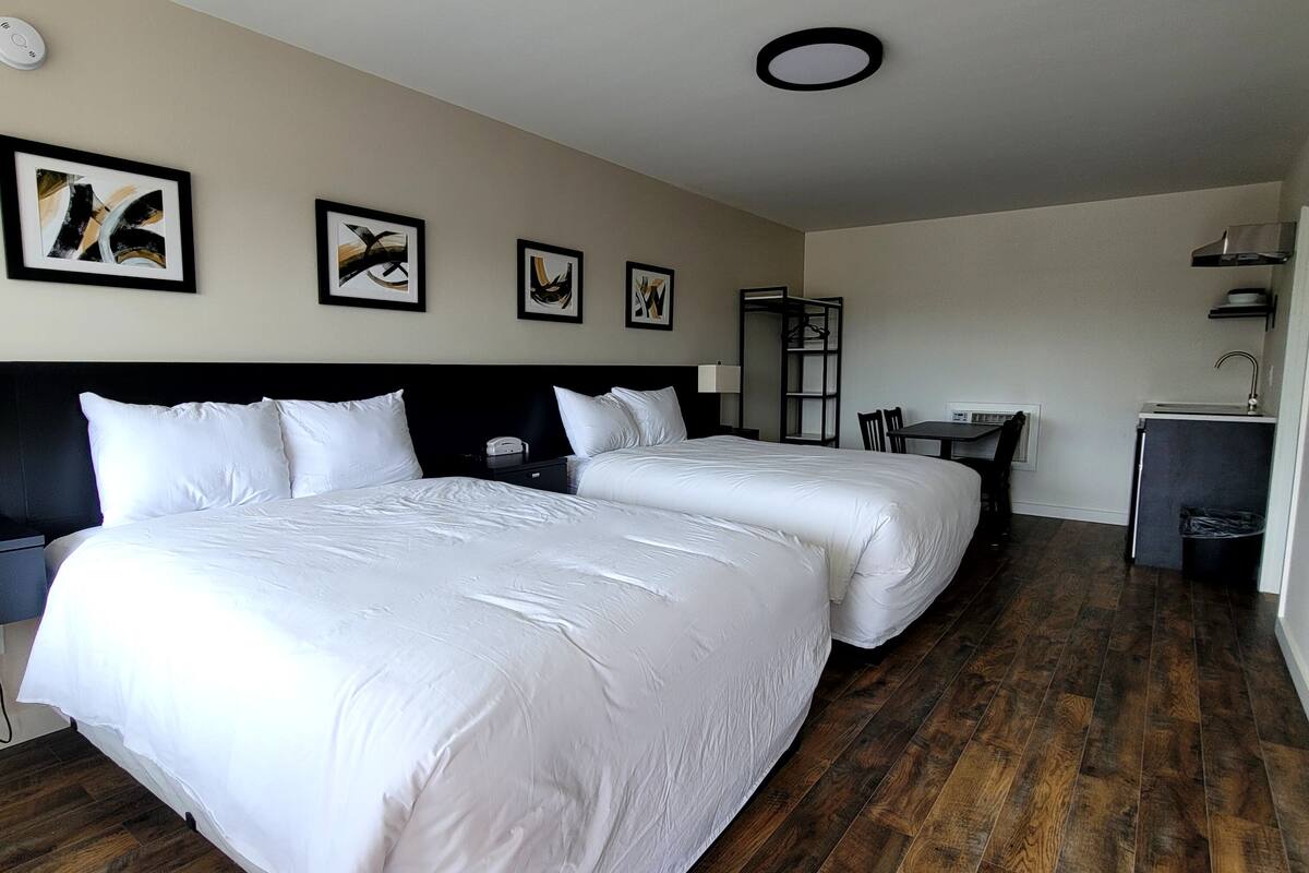 A hotel room with two beds, a desk, a chair, a wardrobe, and a small kitchenette.