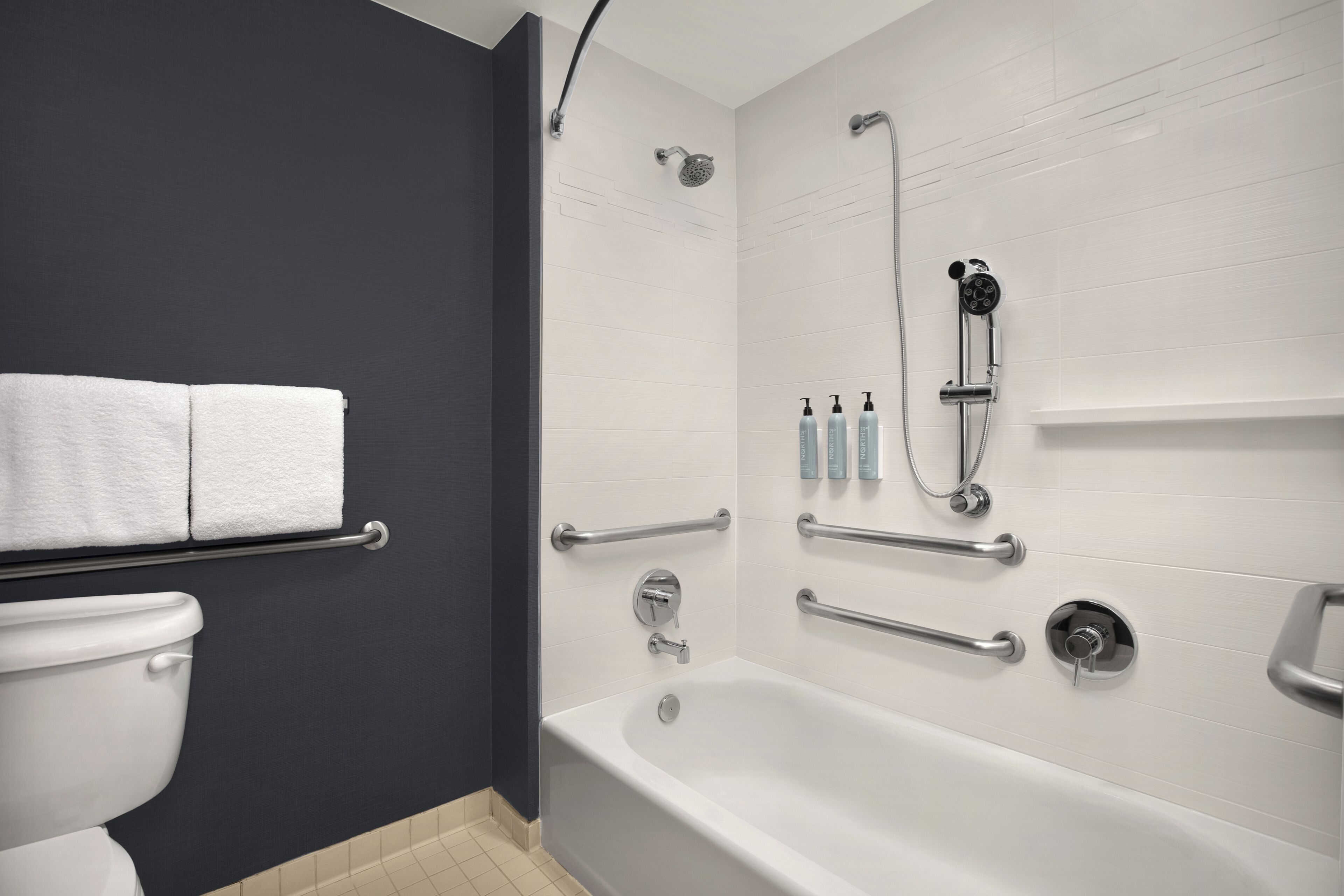 Un baño moderno con bañera, ducha y retrete. Se han instalado barras de apoyo para mayor seguridad.