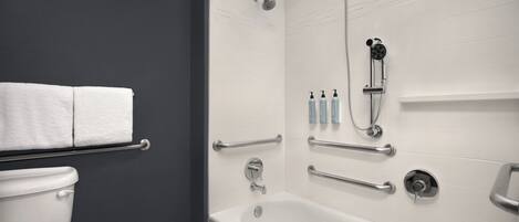 Un baño moderno con bañera, ducha y retrete. Se han instalado barras de apoyo para mayor seguridad.