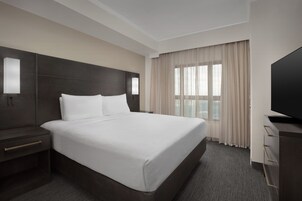 Habitación de hotel con una cama grande, una mesita de noche, un televisor y una ventana con cortinas.