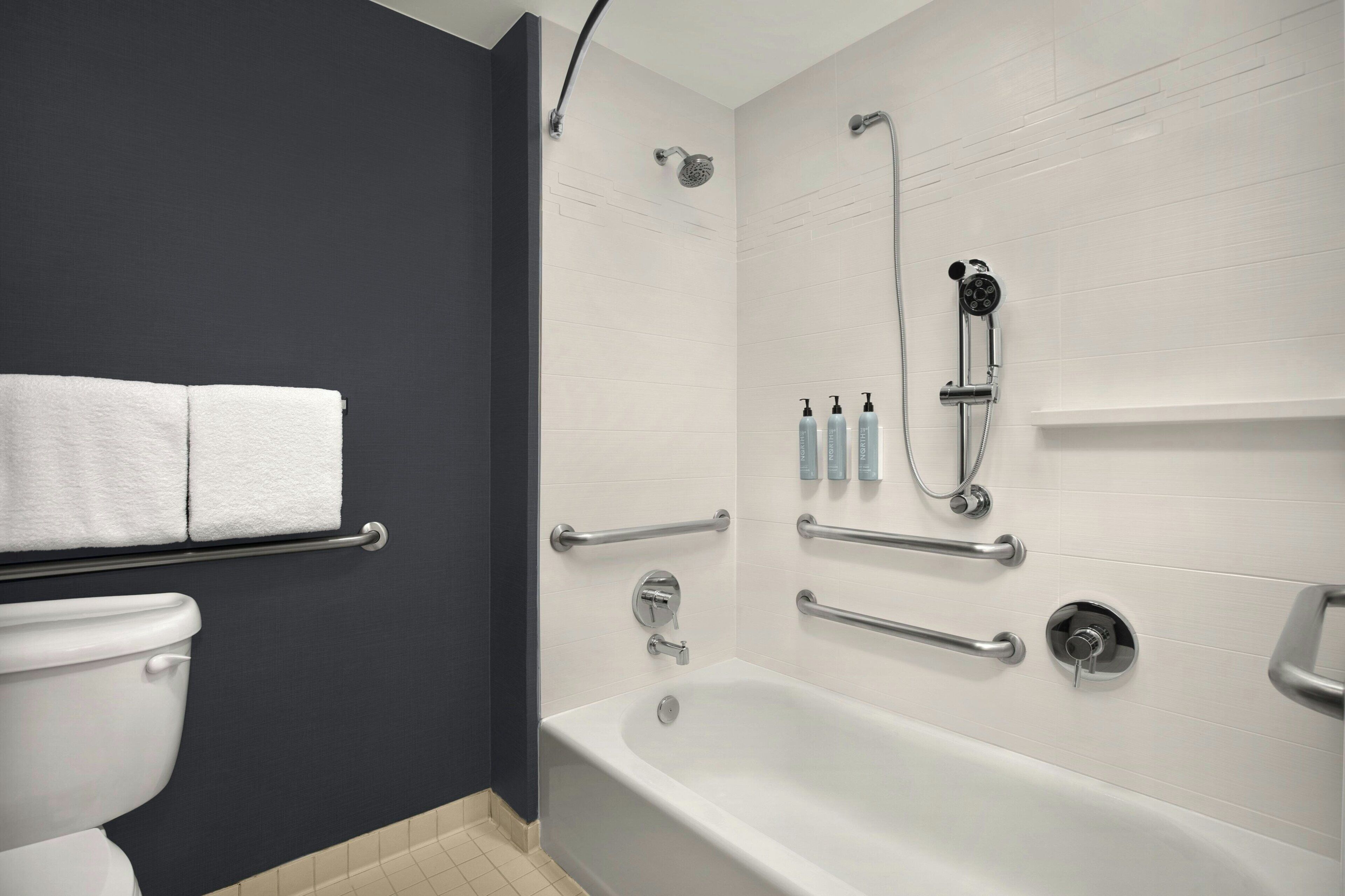 Un bagno moderno con vasca, doccia e servizi igienici. Sono state installate maniglie di sostegno per una maggiore sicurezza.