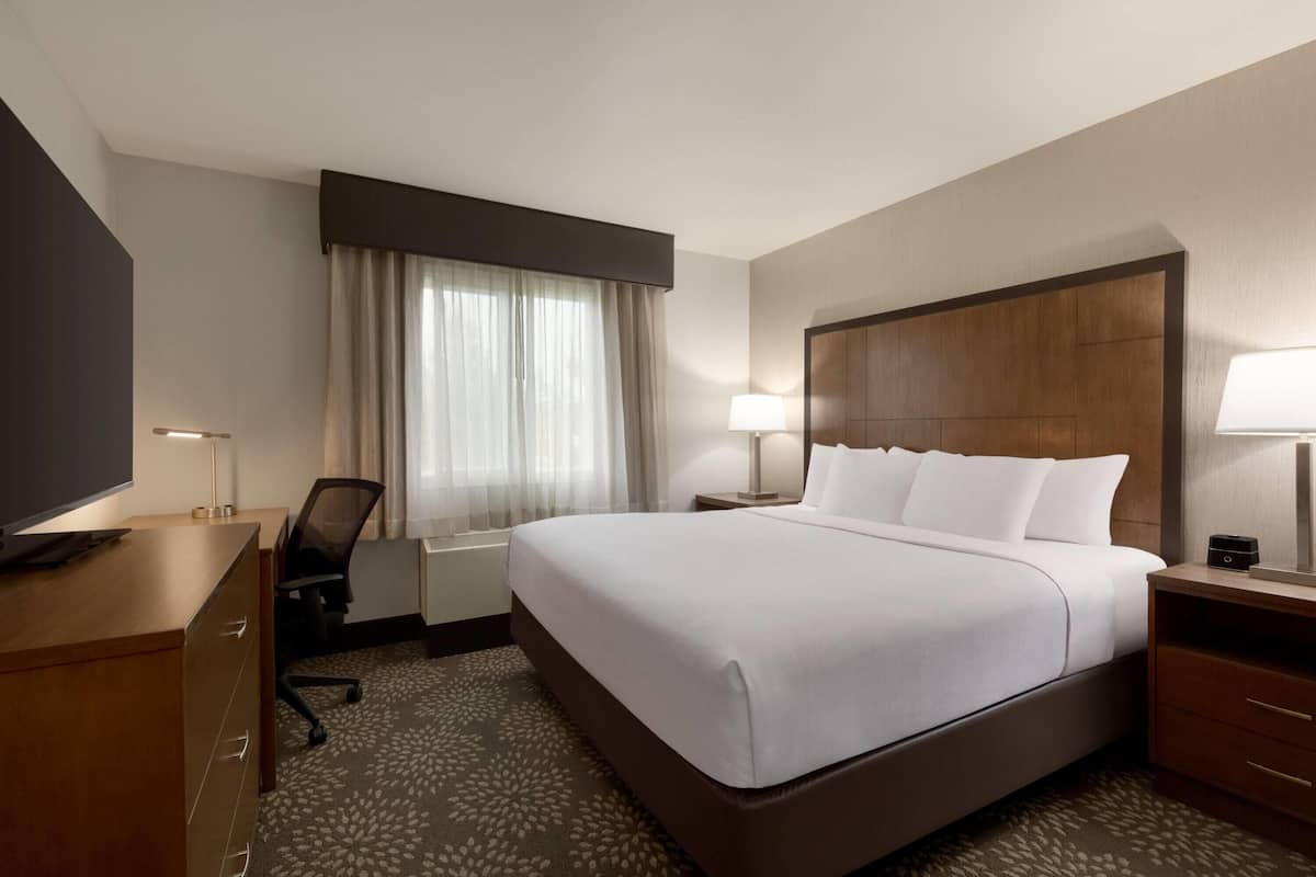 Une chambre d’hôtel avec un grand lit, un bureau avec une chaise, une télévision et une fenêtre avec des rideaux.