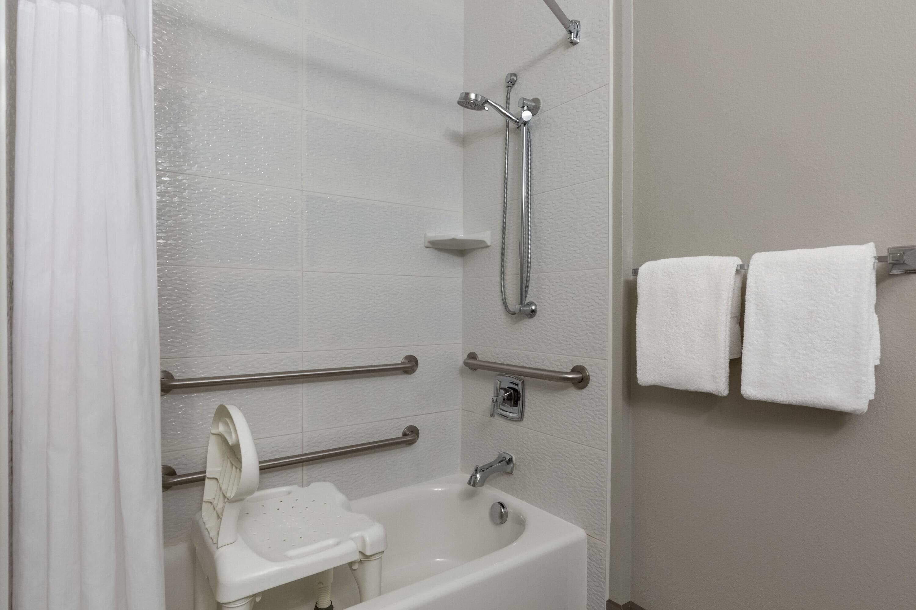 A bathroom with a bathtub, shower, grab bars, and a towel rack.