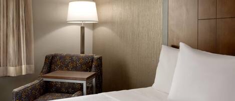 A hotel room with a bed, a chair, a small table, and a lamp.