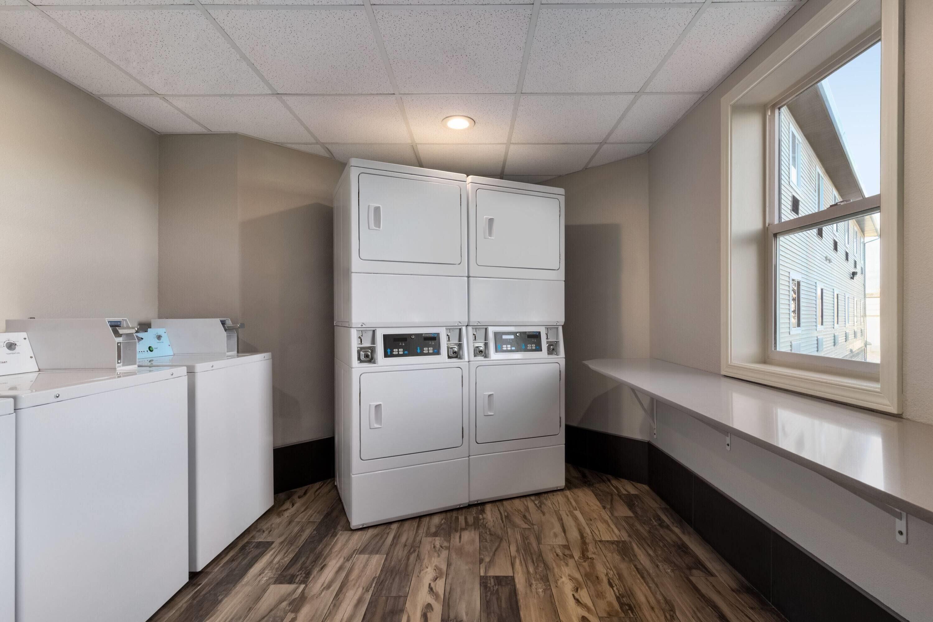 A laundry room with stacked washers and dryers, a window with a view of buildings, and a wooden floor.