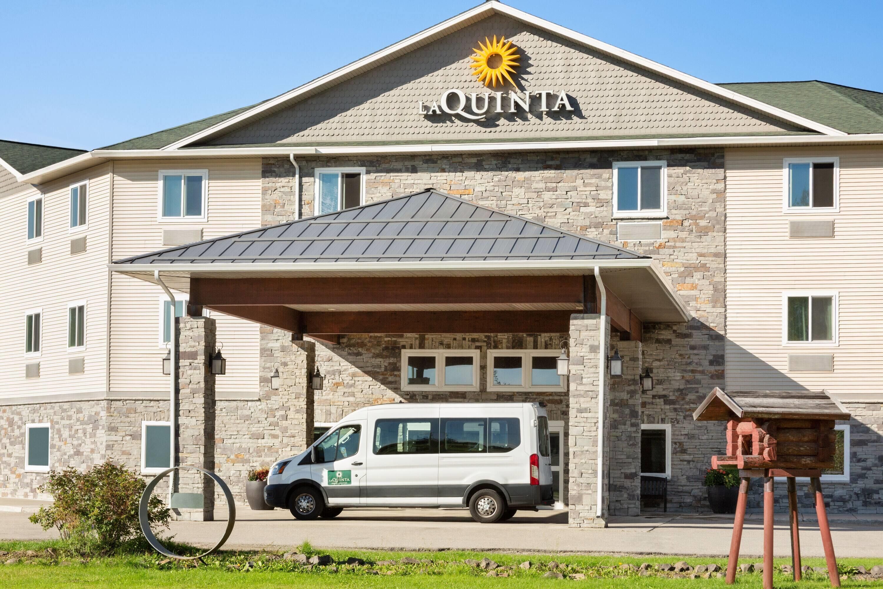 Un hôtel avec une façade en pierre, une entrée couverte et un fourgon garé.