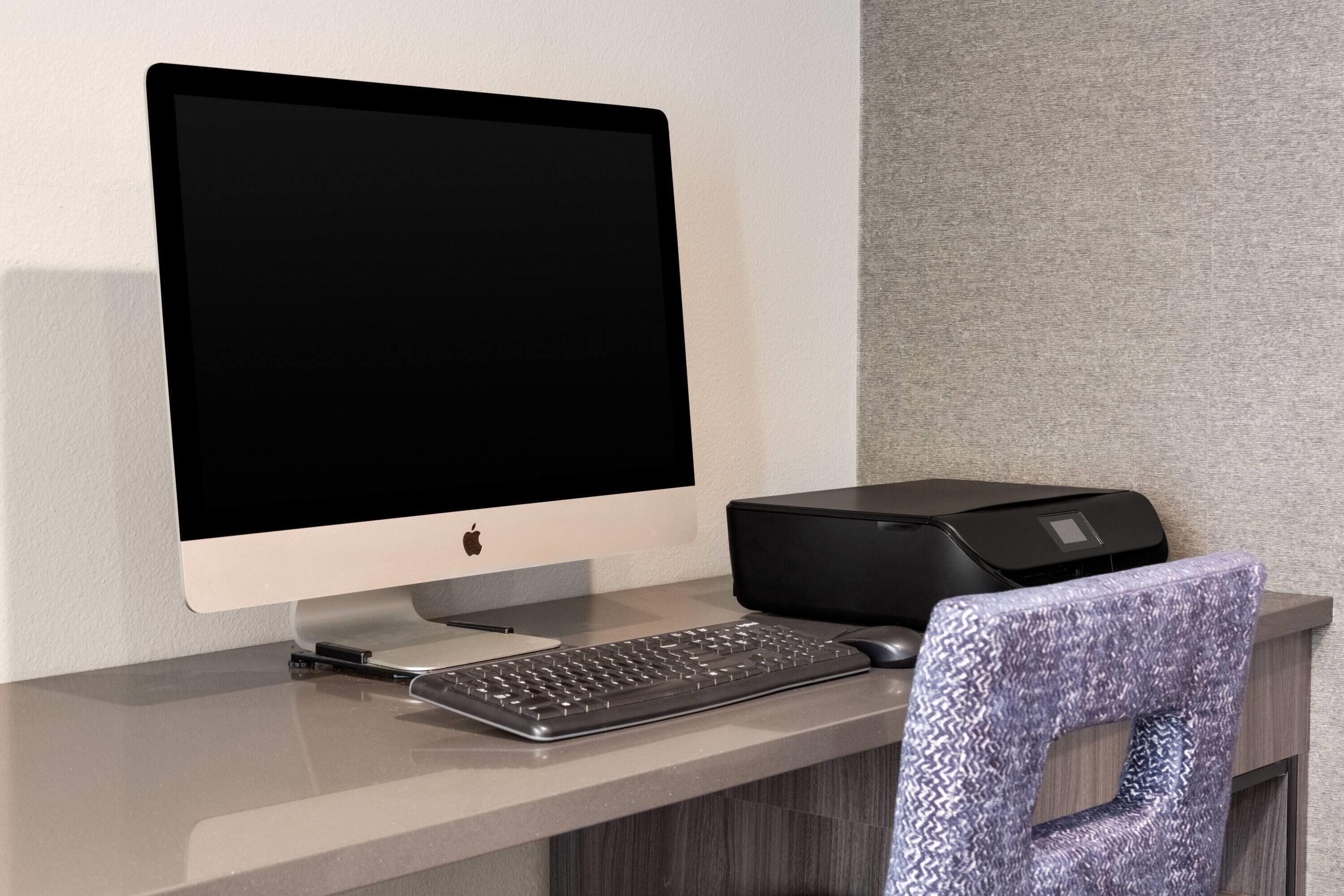 A modern workspace with a desktop computer, keyboard, and printer on a desk.