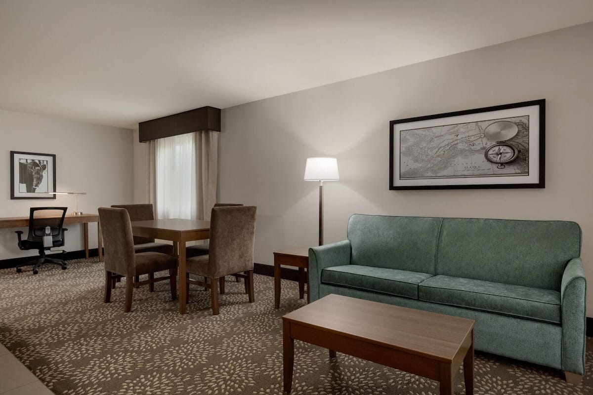 Une chambre d’hôtel équipée d’une table à manger, de chaises, d’un canapé, d’une lampe et d’une carte encadrée accrochée au mur.