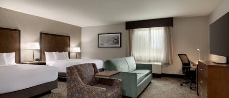 A hotel room with two beds, a sofa, a chair, a desk, and a large window with curtains.