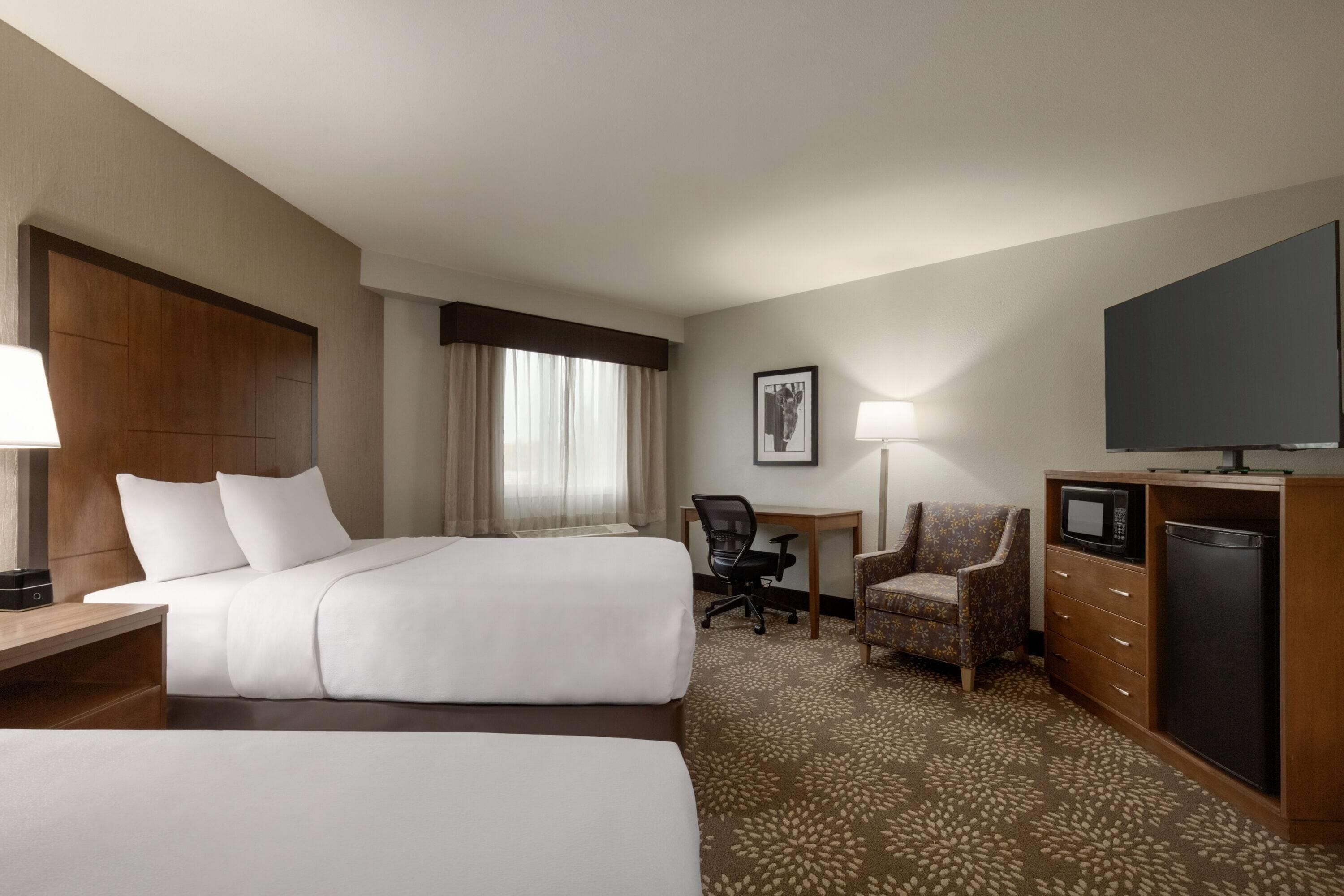 A hotel room with two beds, a desk, a chair, a television, and a microwave.