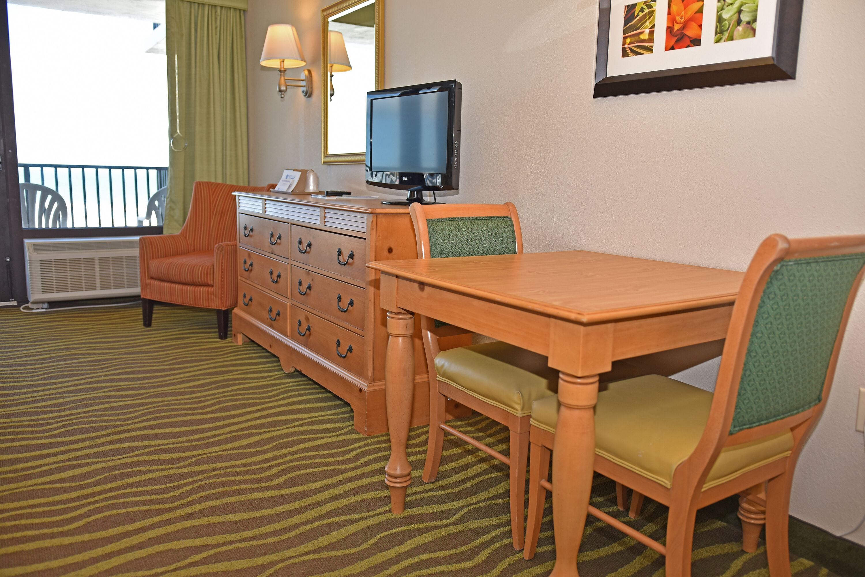 A hotel room with a wooden desk, a television, a dresser, and a chair.