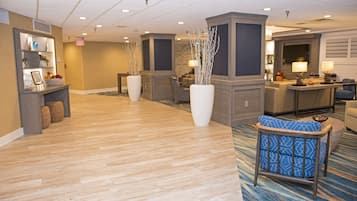A hotel lobby with a reception desk, seating area, and a large vase with branches.