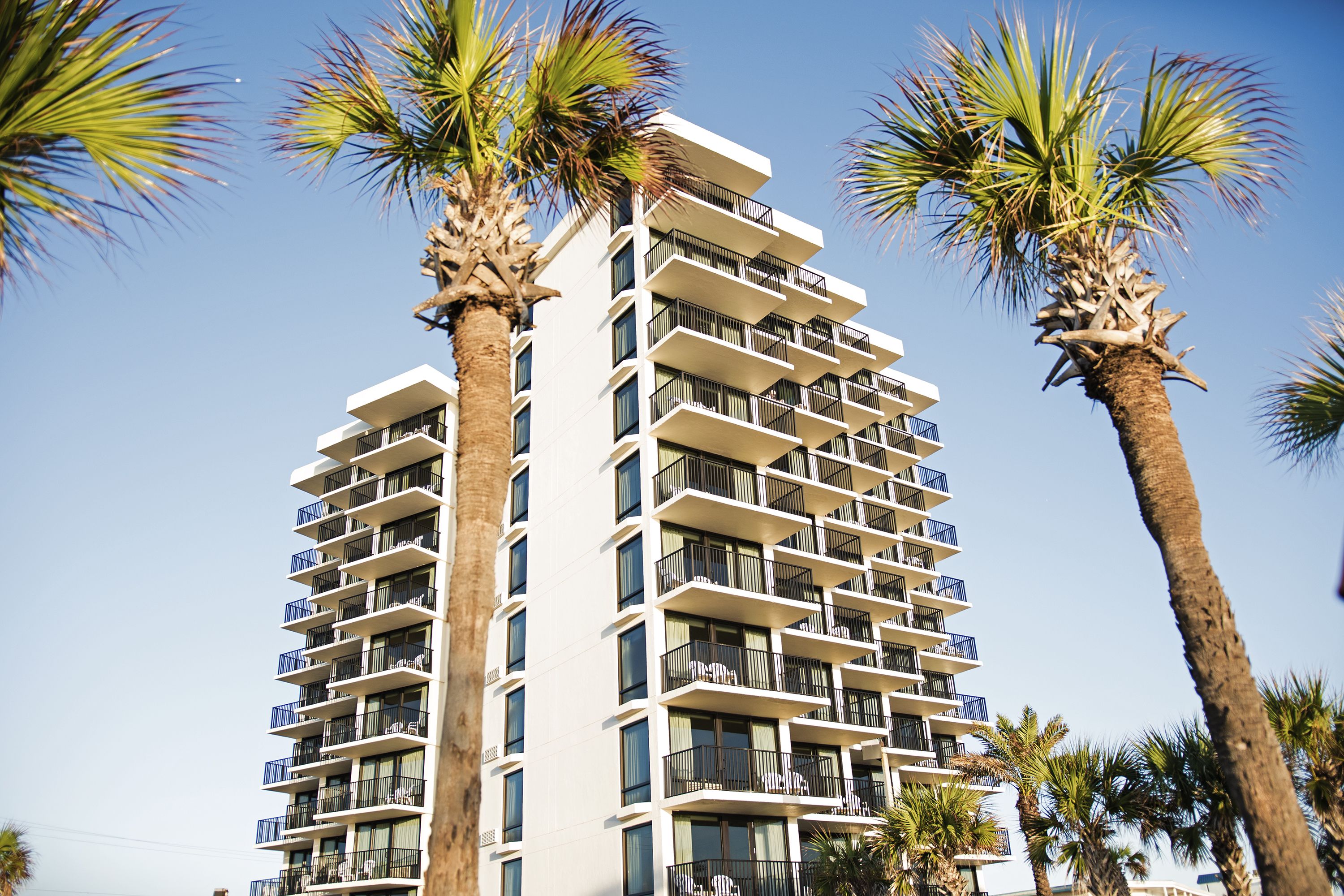 A multi-story hotel with balconies and palm trees.