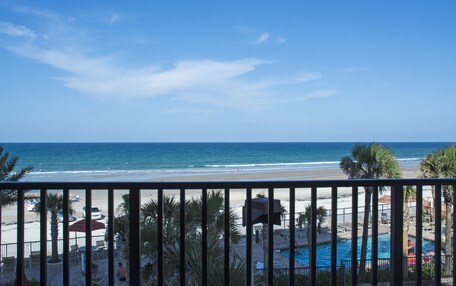 A beach view from a balcony with a pool and lounge chairs.