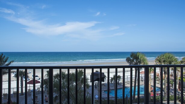 A beach view from a balcony with a pool and lounge chairs.